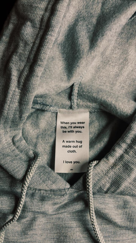 Close-up of hoodie’s inner tag with heartfelt message – “When you wear this, I’ll always be with you. A warm hug made out of cloth. I love you.”