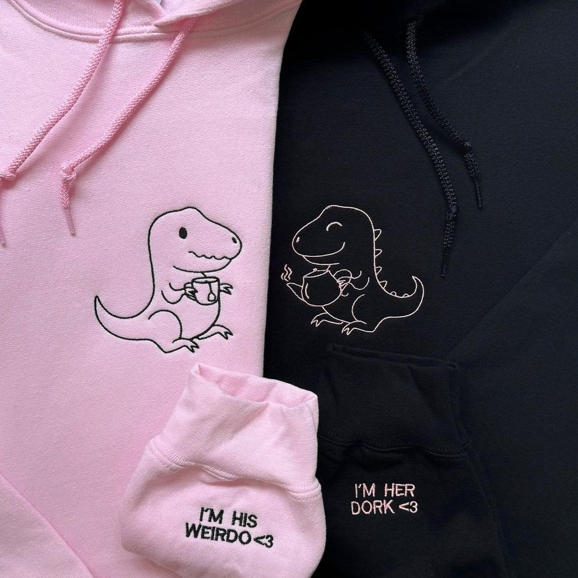 Matching couple hoodies with embroidered dinosaur characters and sleeve text – “I’m his weirdo” and “I’m her dork.”