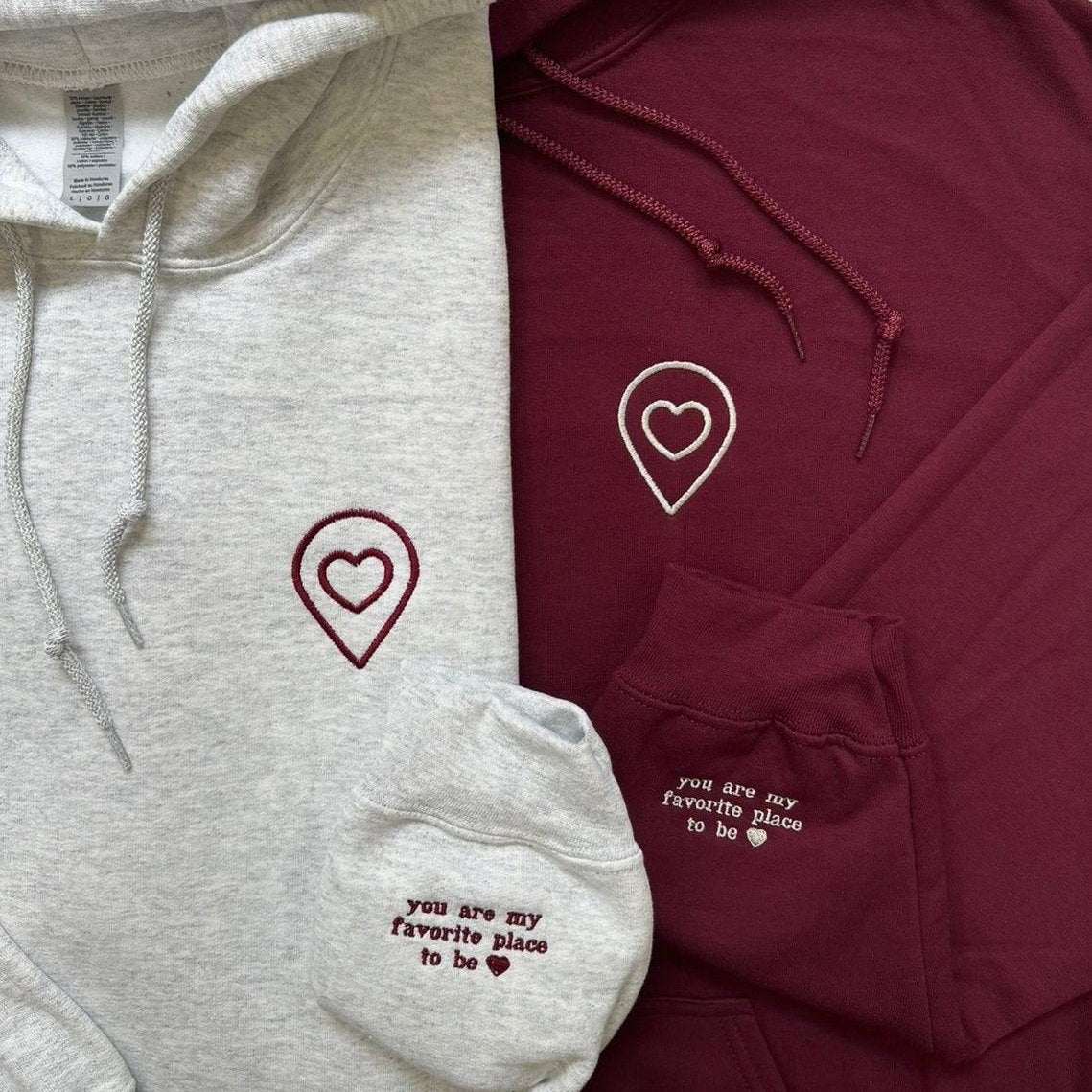 Matching couple hoodies with embroidered heart location icons and sleeve message “You are my favorite place to be.”