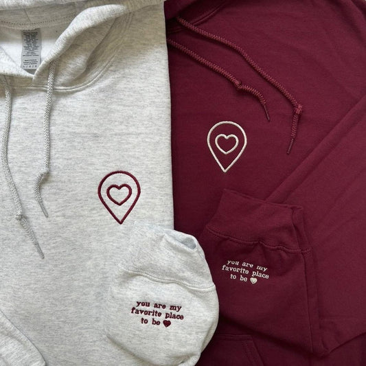Matching couple hoodies with embroidered heart location icons and sleeve message “You are my favorite place to be.”