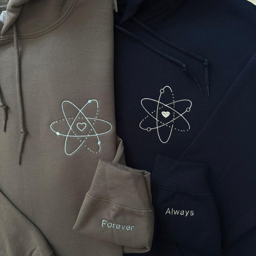Matching couple hoodies with embroidered atom symbols and sleeve messages – “Forever” and “Always” with a heart at the center.