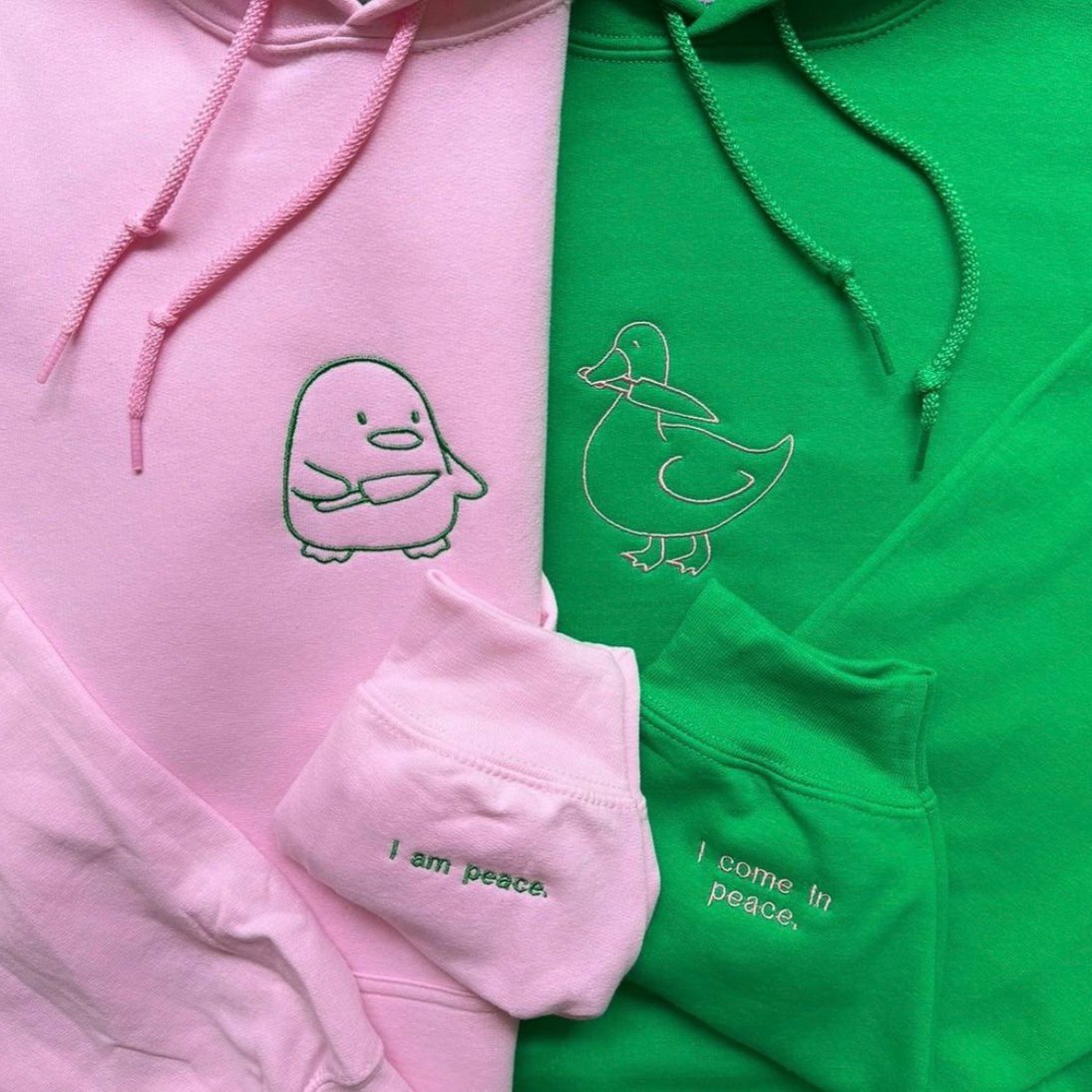 Matching couple hoodies with embroidered cartoon characters and sleeve messages – “I am peace” and “I come in peace.”