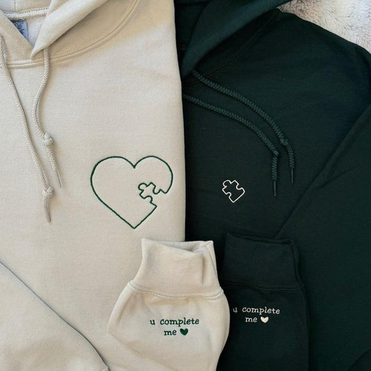 Matching couple hoodies with heart puzzle embroidery and sleeve text “u complete me ♥” on each hoodie.